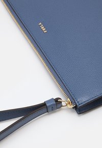 Modrý kožený psaníčko s texturovaným povrchem, zlatým zipem a odnímatelným tmavě modrým zápěstním páskem. Obsahuje zlaté logo značky.