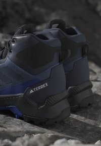 Mörkblå vandringsskor tillverkade av syntetiska material, med en texturerad ovandel, gummisula och uttalad grepp för stabilitet.