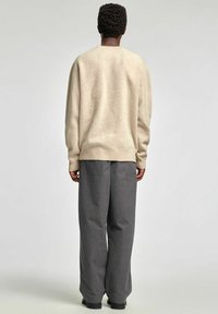 Bézs krāsas oversize džemperis ar apaļu kakla izgriezumu, kopā ar vaļīgām pelēkām svītrainām biksēm. Teksturēta auduma apakšdaļa un aproces ar ribveida rakstu.