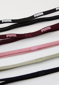 PUMA hiuslenkit mustana, viininpunaisena, vaaleanpunaisena, oliivinvihreänä ja tummanvihreänä; jokaisessa on integroitu logo ja vahvaa, joustavaa kangasta.