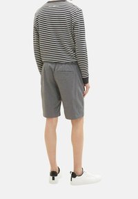 Pantaloni corti a quadri grigi con vita elastica, abbinati a una maglietta a maniche lunghe bianca e nera a righe, e scarpe da ginnastica bianche con dettagli neri.