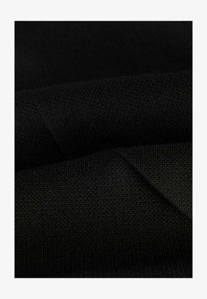 Černá látka s texturovaným pleteným vzorem, na které jsou vidět záhyby a vrásky. Materiál se jeví jako měkký a hustý, což zdůrazňuje hladký povrch.