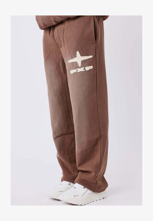 Bruine katoenen joggingbroek met zijzakken, voorzien van een wit logo en grafische details. Gecombineerd met witte sneakers voor contrast.