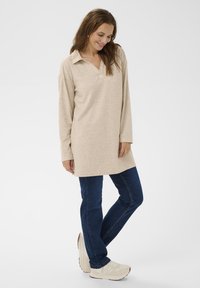 Bežna tunika s long sleevima i kragnom, udobnog kroja, u kombinaciji s tamnoplavim trapericama i svijetlim tenisicama. Jednostavna, glatka tekstura.