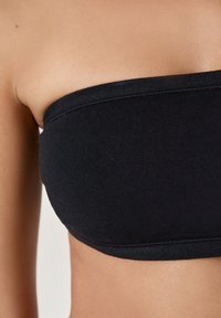 Top bandeau nero senza spalline in tessuto morbido. Texture liscia con un design aderente, caratterizzato da un bordo pulito e senza cuciture e dettagli di cucitura minimi.