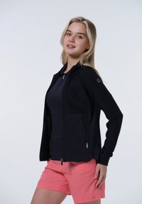 Marinblå zip-up jacka med strukturerade ribbade paneler, i kombination med rosa shorts. Har en figursydd design och fickor. Lättviktig, sportig material.