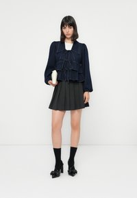 Marineblauwe denimjas met ruches en strikdetails, gecombineerd met een geplisseerde donkergrijze rok. Complementeert: zwarte strik-hakken en kniehoge sokken.
