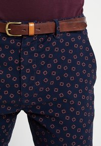 Marineblauwe gebloemde broek met kleine rode vierkantjes, voorzien van een bruine leren riem met een gouden gesp, van katoen en met een rechte snit.