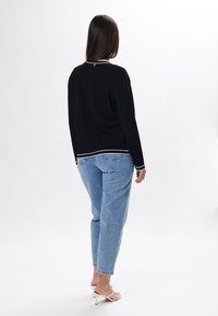 Top negro de manga larga con ribete blanco en el dobladillo, combinado con Jeans de mezclilla azul claro. Textura suave, ajuste relajado y calzado de fácil poner.