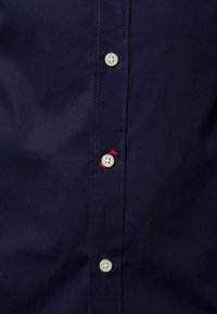 Navy blue shirt featuring a front placket with light buttons, contrasting red stitching, and smooth fabric texture.