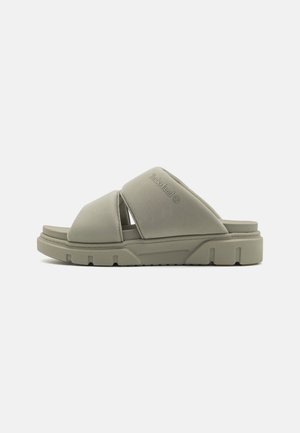 Beige slip-on sandal med tykke krydsede remme og en robust, tekstureret sål, med et diskret Timberland-logo på den øverste rem.