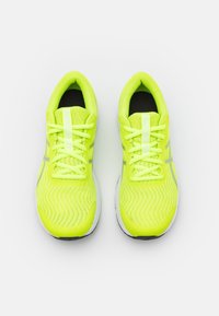 Neon žluté sportovní boty s texturovaným síťovaným svrškem, plochými tkaničkami, reflexními prvky a bílou gumovou podrážkou.