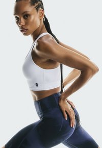 Sujeta deportivas blanca con un logo en el lateral, combinada con leggings azul marino de cintura alta. Tejido suave y elástico con un ajuste elegante.