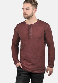 Langærmet bordeaux henley skjorte med fem knapper ved halsen og et tekstureret, let falmet stof. Parret med mørke jeans.