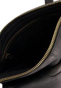 Schwarze Lederhandtasche mit goldenem Reißverschluss, ausgestattet mit einer glatten Oberfläche und einem mit Reißverschluss versehenen Innenfach. Markenname ist im Inneren sichtbar.