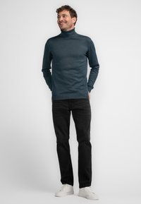 Granatowy golf z miękkiego materiału, w połączeniu z czarnymi dżinsami i białymi trampkami, w odzieży o dopasowanym kroju.