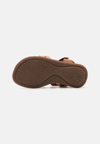 Suela de sandalia marrón con patrón floral; superficie de goma ligeramente texturizada; forma curvada; acentos de color mínimos, incluyendo tirantes rosas a los lados.