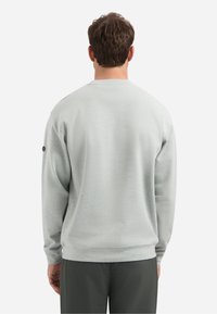 Lichtgrijze sweatshirt met ronde hals, textuurstof en geribbelde mouwen. Een ronde logopatch bevindt zich op de linker schouder.