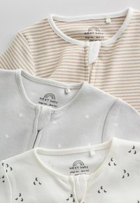 Tre vikta babypyjamas med rundade halslinningar, med beige ränder, vit med stjärnor och vit med svarta månmönster.