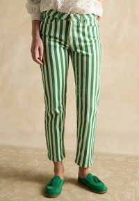 Zelené a biele rifle s vertikálnymi pruhmi a úzkym strihom, s predným zapínaním na gombíky a dvoma bočnými vreckami. Kombinované so zelenými mokasínami.