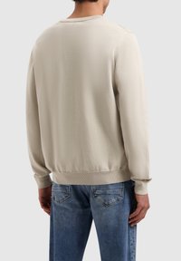 Lichtbeige trui met een ribgebreide halslijn en manchetten, met een zachte textuur en minimale details, gecombineerd met lichtblauwe jeans.