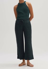 Mörkgrön stickad linne med hög hals, kombinerat med löst sittande, vida grå byxor och platta sandaler med ett rem-design.