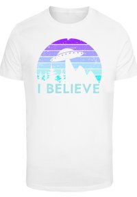 White cotton t-shirt featuring a colorful graphic design of a UFO above mountains and trees, with the text "I BELIEVE" in light blue.