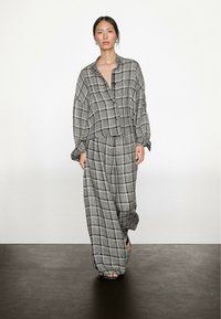 Ternet outfit bestående af en løstsiddende skjorte med knapper og vidde bukser i gråtoner, lavet af et let stof med en blød tekstur.