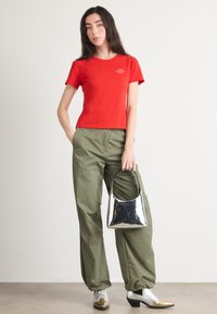 Crvena kratka majica s kratkim rukavima, maslinasto zelene široke hlače, srebrna sjajna torba i metalna obuća s zakrivljenim prstima. Jednostavan, ležeran outfit.