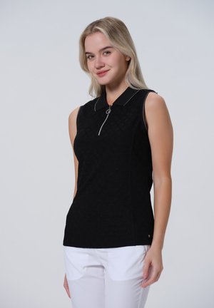 Černý bezrukávový polo top se zipem na límci, se strukturovaným vzorem a kontrastním bílým lemem. Spárovaný s bílými kalhotami.