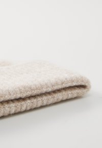 Beige villane kangas, volditud, näidates pehmet tekstuuri, millel on kerge läige ja peenene karvane välimus. Servad on korralikult lõpetatud.