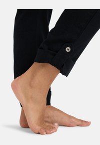 Dark denim pants with a cuffed hem and a silver button detail. A bare foot is positioned alongside the pant leg, showcasing skin tone.