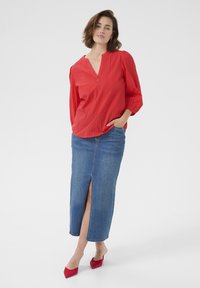 Röd långärmad blus med V-hals och vertikal randtextur, ihopparad med en figurnära, knä-lång denimkjol med hög slit framtill.