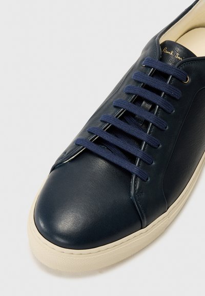 Sapatilha de couro azul-marinho com atacadores planos azul-marinho, design simplificado e sola de borracha texturizada branca. O interior apresenta forro bege.