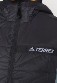 Schwarze gesteppte Jacke mit Kapuze, ausgestattet mit einem Frontreißverschluss, elastischen Besätzen und dem Wort "TERREX" in Grau auf der Brust.