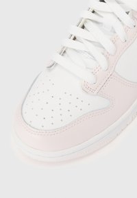 Tuvojoties baltā un gaiši rozā sporta apaviem, to purngala daļa ir izgatavota no perforētas ādas, un ir balti apavi. Fons ir vienkrāsains.