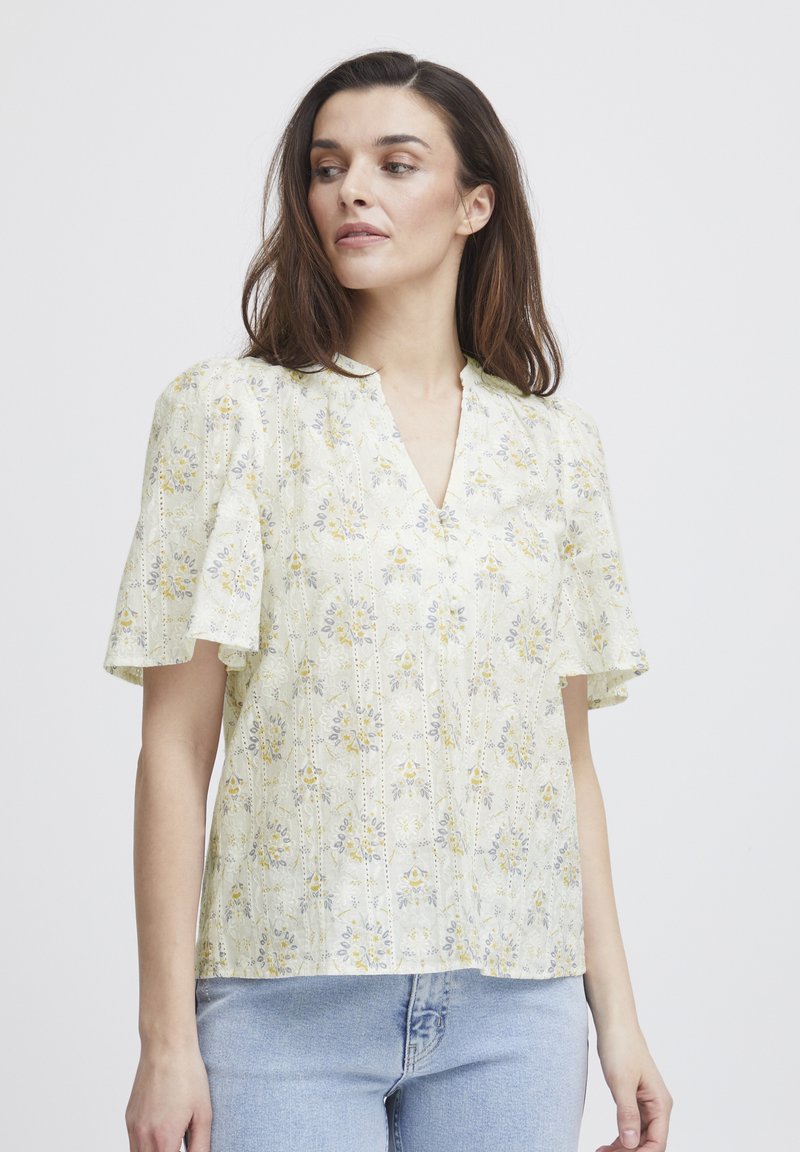 Kortärmad blus med V-ringning i ljusgul tyg. Har blommönster i blått och gult, med texturerade detaljer och en avslappnad passform.