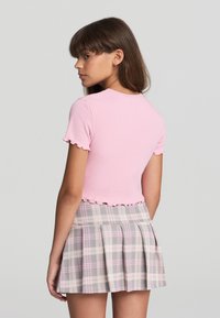 Top corto a maniche corte rosa a righe con orlo scallop, abbinato a una gonna plissettata a quadri grigia con accenti rosa.