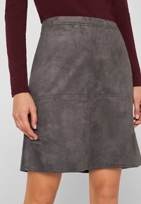 Jupe A-line en daim gris avec une texture lisse, présentant une taille ajustée et des détails de couture subtils le long des coutures latérales.