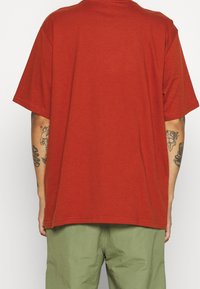 T-shirt en coton rouge à manches courtes et coupe décontractée. Il présente un col rond et est assorti à un pantalon vert.