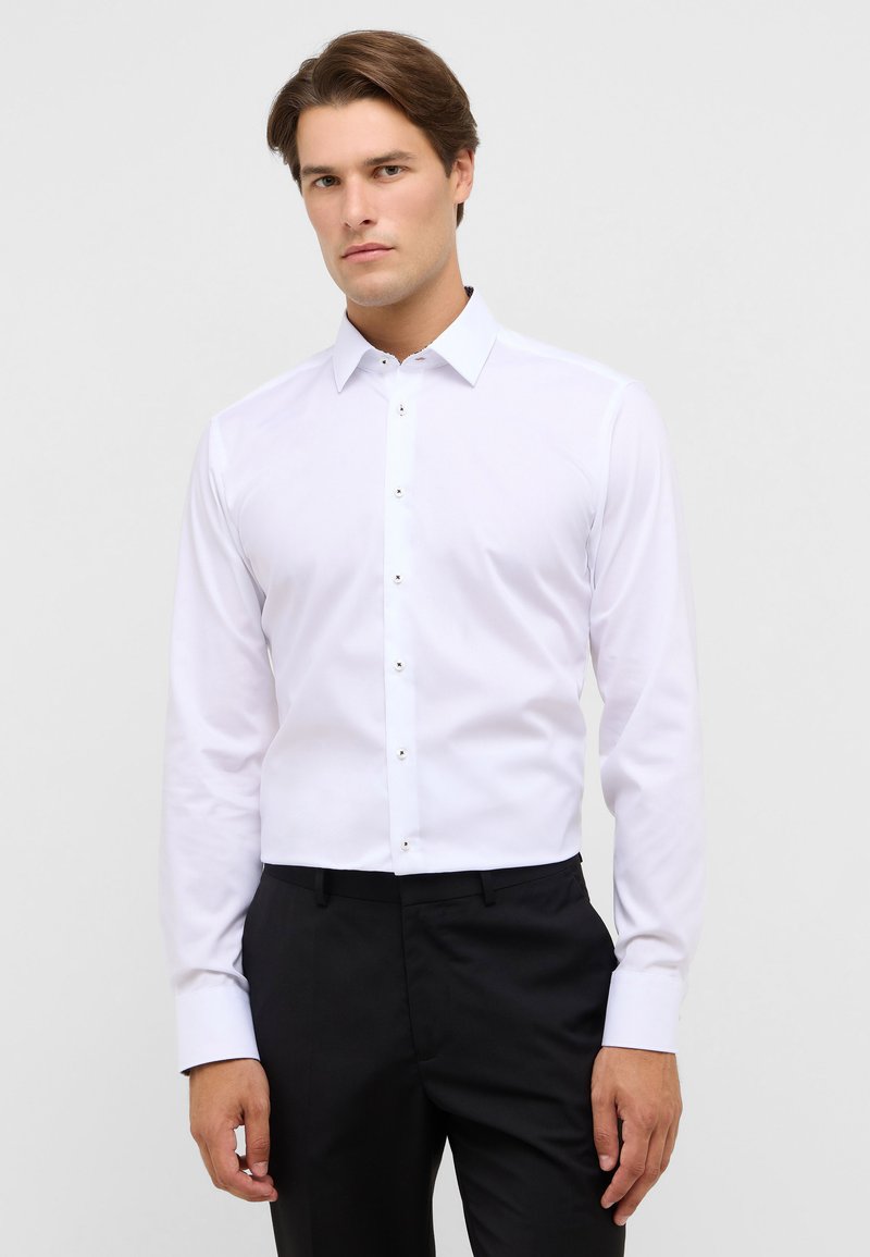 Witte blouse met lange mouwen, een gespreide kraag, knoopsluiting en contrasterende knoopaccenten, gecombineerd met zwarte broek. Soepele stoftextuur.