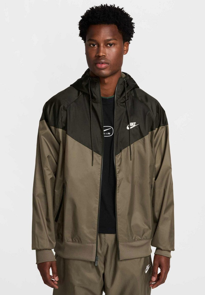 Kurtka Nike typu zip-up w jasno-oliwkowym i ciemno-oliwkowym kolorze. Posiada kaptur, elastyczne mankiety oraz wykończenie. Logo na piersi. Gładki, lekki materiał.