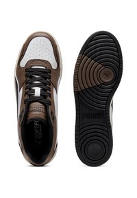 Braune und weiße Sportschuhe mit schwarzen strukturierten Schnürsenkeln, die über perforierte Details, ein weiches Lederobermaterial und eine Gummisohle mit kreisförmigem Profil verfügen.
