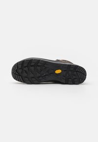 Hiking schoen zool in zwart rubber, met diepe noppen voor grip. Het hielgebied toont een geel logo-accent nabij het midden.