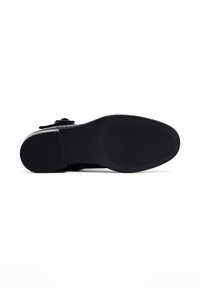 Semelle de chaussure noire avec un grip en caoutchouc texturé, forme contournée et légère courbure au niveau des orteils. Présente un design épuré sans logos visibles.