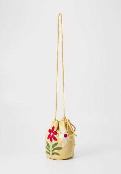 Κίτρινη τσάντα με κορδόνι από ύφασμα με λουλουδάτη κεντημένη διακόσμηση σε κόκκινο, άσπρο και πράσινο, με στρογγυλή βάση και μακρύ λουρί για τον ώμο.