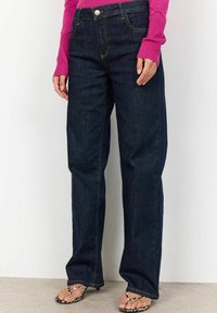 Mörkblå denimjeans med rak bendesign. Har gula sömmar och en framficka med metallknappstängning.