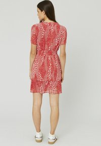 Robe courte rouge avec un motif floral blanc, manches courtes, taille froncée, ourlet en couches, associée à des baskets blanches. Texture de tissu lisse.