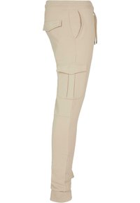 Beige cargo pants made of soft material, featuring side pockets, elastic waistband, and cuffed ankles. Smooth texture with stitching details.
