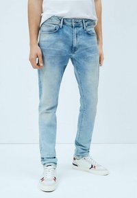 Vaaleansiniset farkut slim fit -mallilla, viidellä taskulla ja haalistuneella pesulla. Yhdistetty valkoisiin lenkkareihin, joissa on punaisia ja laivastonsinisiä yksityiskohtia.